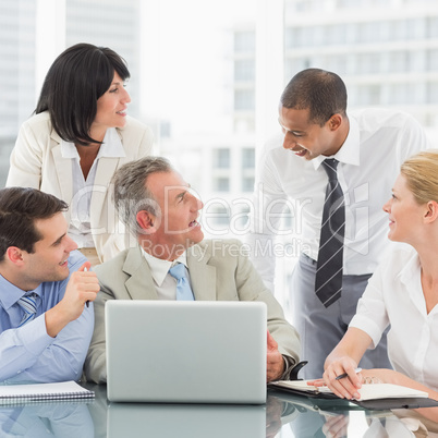 Happy business team gathered around laptop chatting