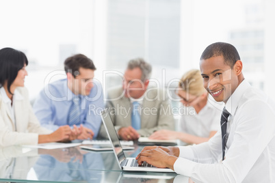 Businessman using laptop during a meeting smiling at camera