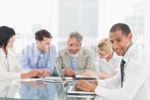 Businessman using laptop during a meeting smiling at camera