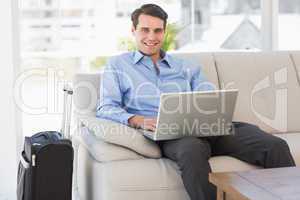 Travelling businessman using laptop sitting on the couch smiling