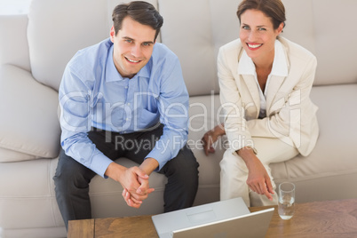 Happy business partners looking at camera sitting on sofa