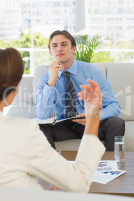 Young businessman listening to female colleague sitting on couch