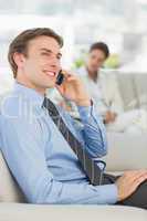 Happy businessman on the phone sitting on sofa