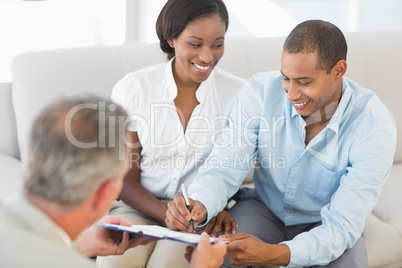 Young smiling couple signing contract on the couch