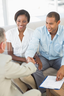 Young smiling couple shaking hands with salesman on the couch