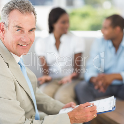 Salesman smiling at camera with couple behind him