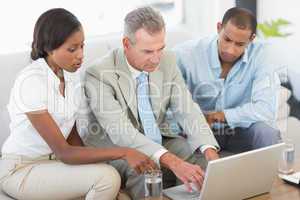 Salesman showing something on laptop to couple on sofa