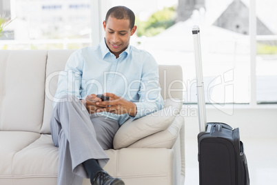 Man sitting on sofa sending a text waiting to depart on business