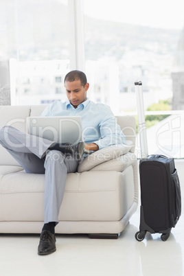 Businessman using laptop sitting on sofa waiting to depart on bu