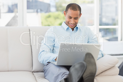 Happy businessman using laptop with his feet up