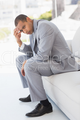 Worried businessman sitting on couch with head in hand looking a