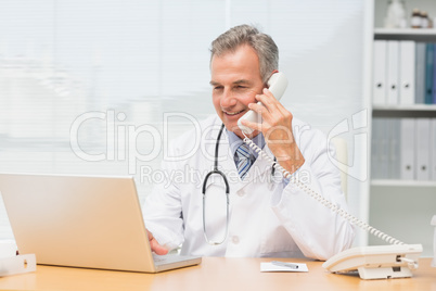 Doctor using laptop and talking on phone at desk
