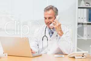 Doctor using laptop and talking on phone at desk