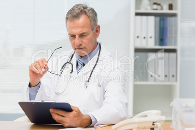 Concentrating doctor sitting at his desk with clipboard