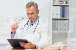 Concentrating doctor sitting at his desk with clipboard