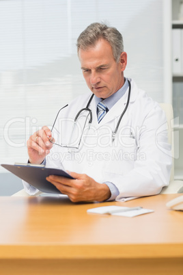Concentrating mature doctor sitting at his desk with clipboard