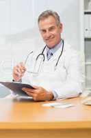 Smiling doctor sitting at his desk with clipboard