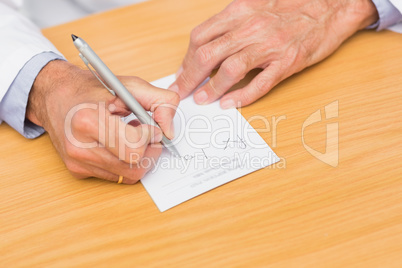 Doctor sitting at his desk writing on prescription pad