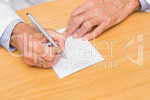 Doctor sitting at his desk writing on prescription pad