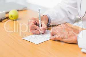 Doctor sitting at his desk writing out a prescription