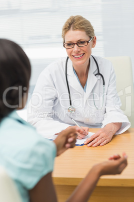 Smiling doctor listening to her patient and taking notes