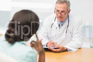 Mature doctor listening to his patient and taking notes
