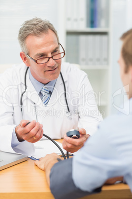 Smiling mature doctor taking his patients blood pressure