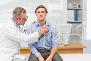 Mature doctor listening to his patients chest with stethoscope