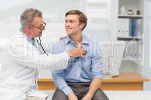 Mature doctor listening to his happy patients chest with stethos
