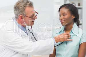 Doctor listening to cheerful young patients chest with stethosco