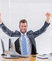 Cheerful businessman clenching fist at office desk