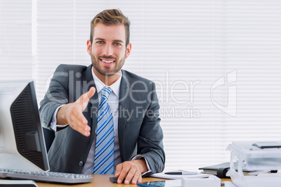 Businessman offering a handshake at office desk