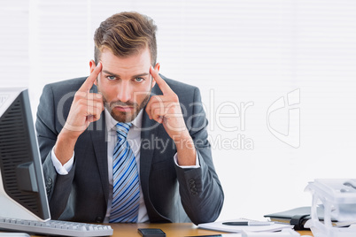 Elegant businessman with headache at office desk