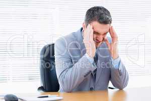 Businessman with severe headache at office desk