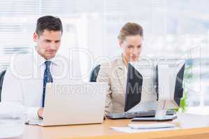 Smartly dressed colleagues using computer and laptop