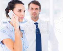 Woman on call with colleague in background at office