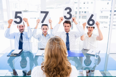 Group of panel judges holding score signs in front of a woman