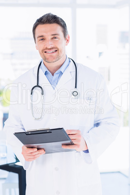 Confident male doctor with clipboard in hospital