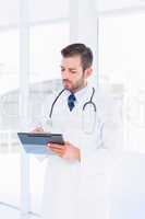 Concentrated male doctor writing reports in clipboard