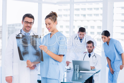 Doctors examining x-ray with colleagues using laptop behind