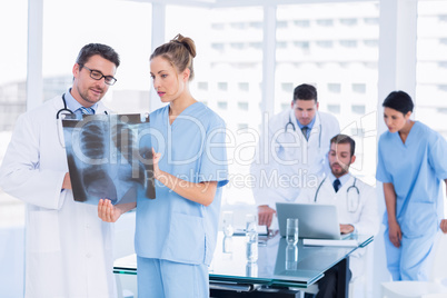 Doctors examining x-ray with colleagues using laptop behind