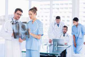 Doctors examining x-ray with colleagues using laptop behind