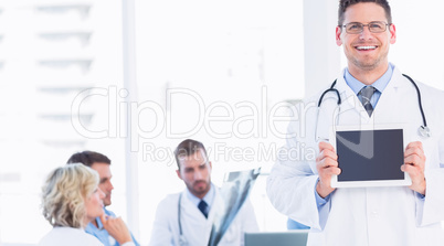Doctor holding digital tablet with colleagues in meeting