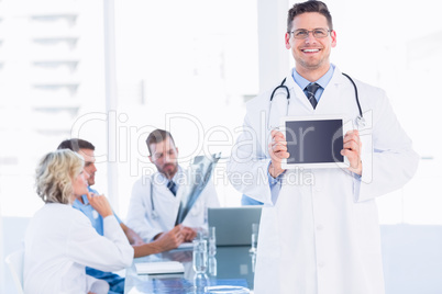 Doctor holding digital tablet with colleagues in meeting