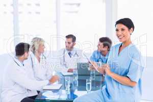 Female surgeon using digital tablet with colleagues in meeting