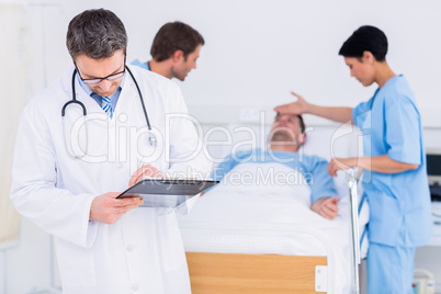 Doctor writing reports with patient and surgeon in background