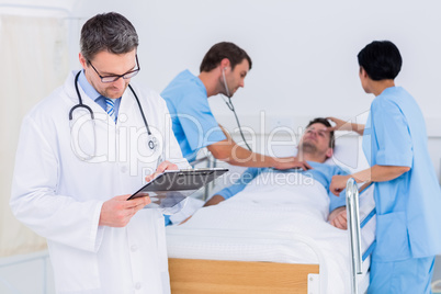 Doctor writing reports with patient and surgeons in background