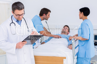 Doctor writing reports with patient and surgeons in background