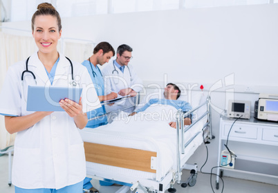 Doctor using digital tablet with colleagues and patient behind