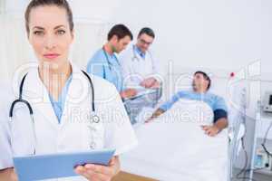 Doctor using digital tablet with colleagues and patient behind